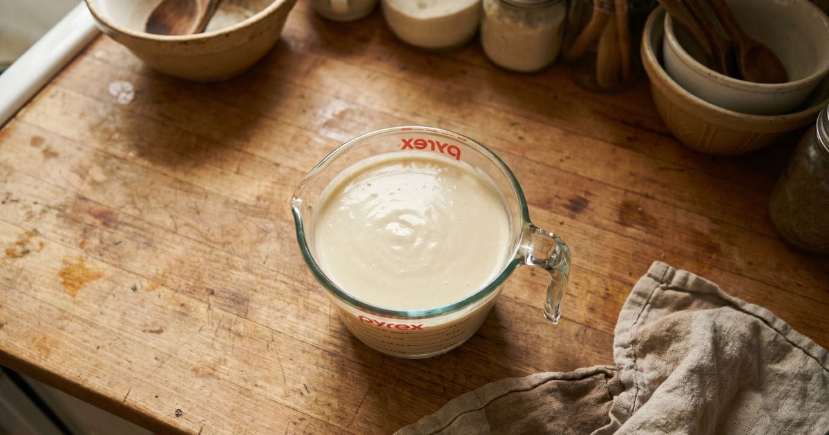 Homemade cream of chicken soup substitute in a glass measuring cup on a weathered wood counter