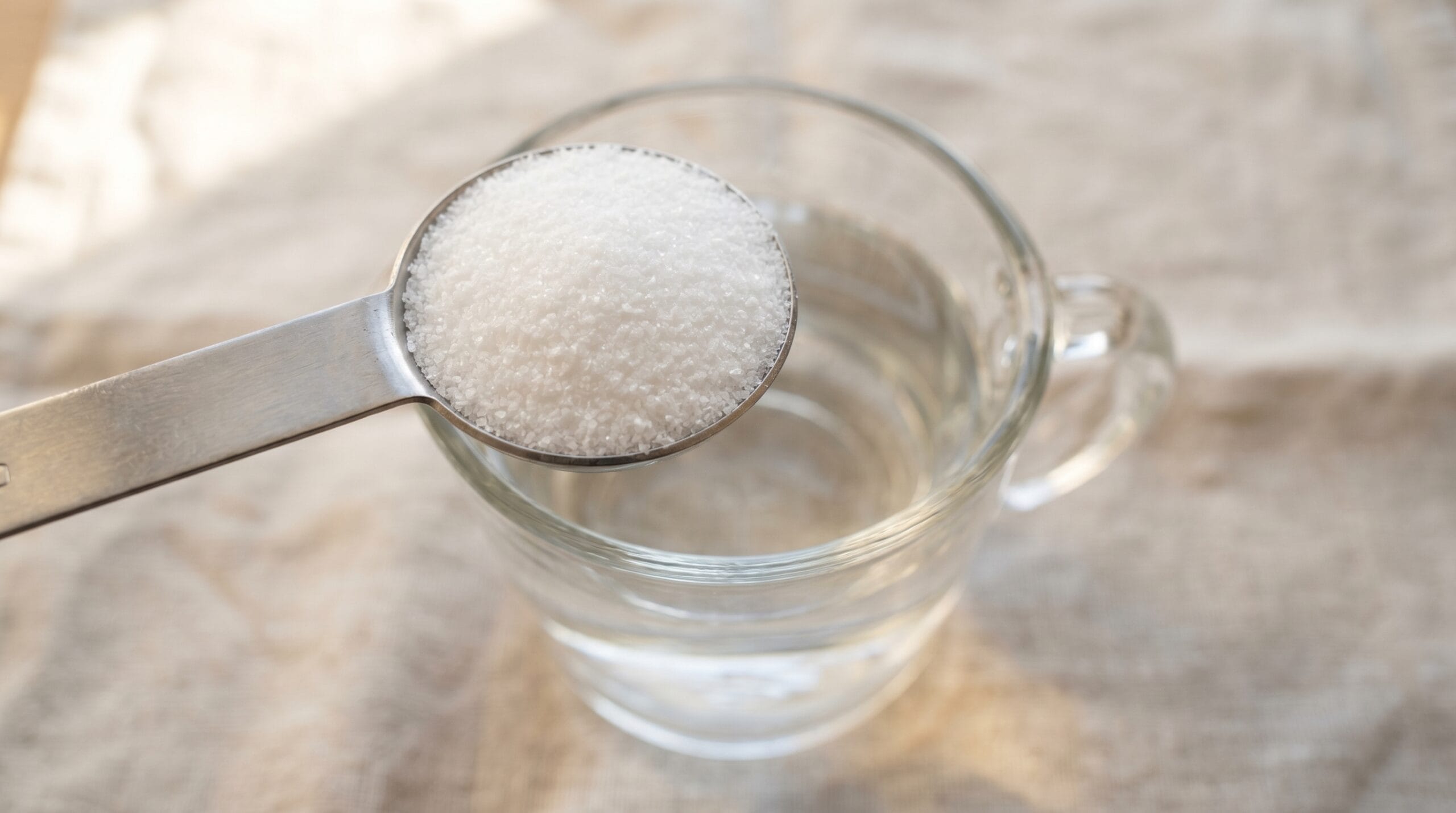 A level tablespoon of white pickling salt in a measuring spoon held over a glass measuring cup of water