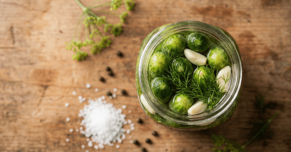 Wide-mouth mason jar packed with small cucumbers, fresh dill, and garlic on a wooden surface