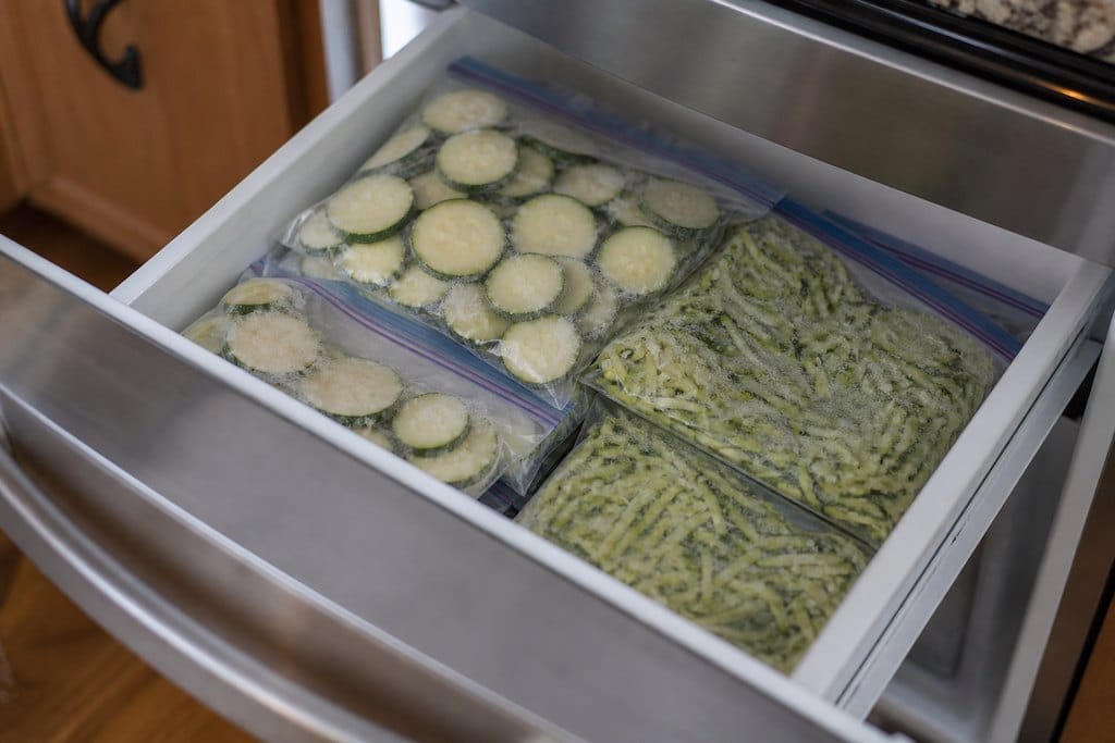 Flat freezer bags of sliced and shredded zucchini stacked on a freezer shelf